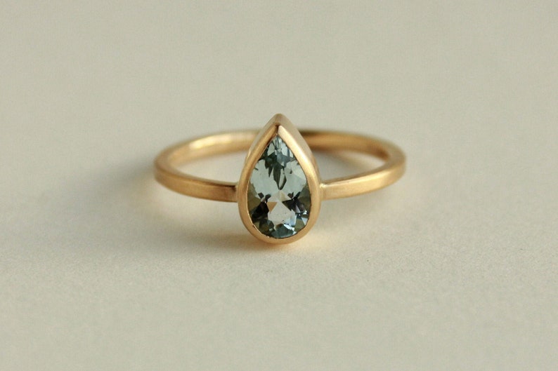 May include: A gold ring with a pear-shaped aquamarine gemstone.