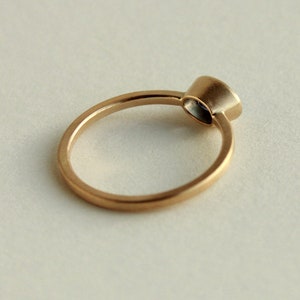 May include: A simple gold band ring with a single round gemstone set in a bezel setting.