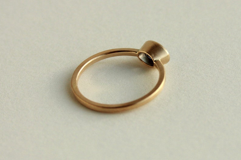 May include: A simple gold band ring with a single round gemstone set in a bezel setting.