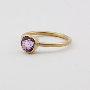 May include: A delicate gold ring with a single round, light purple gemstone set in the center.