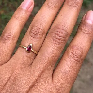 May include: A gold ring with a teardrop-shaped red gemstone.