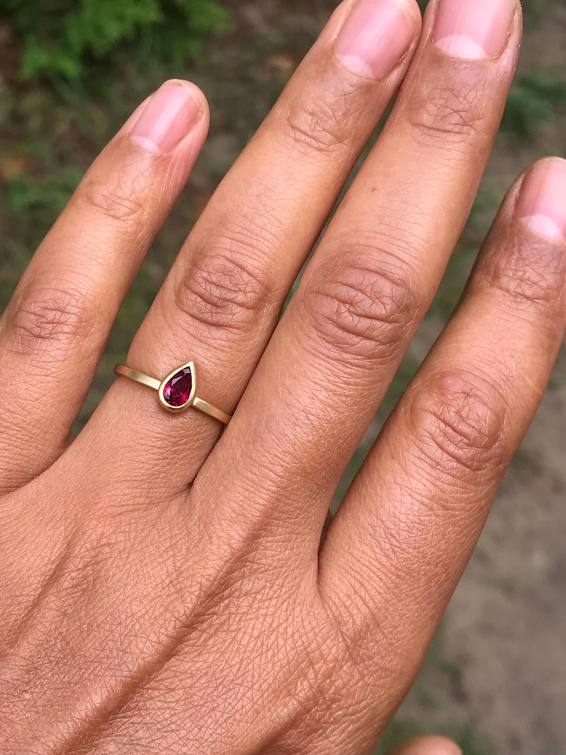 May include: A gold ring with a teardrop-shaped red gemstone.