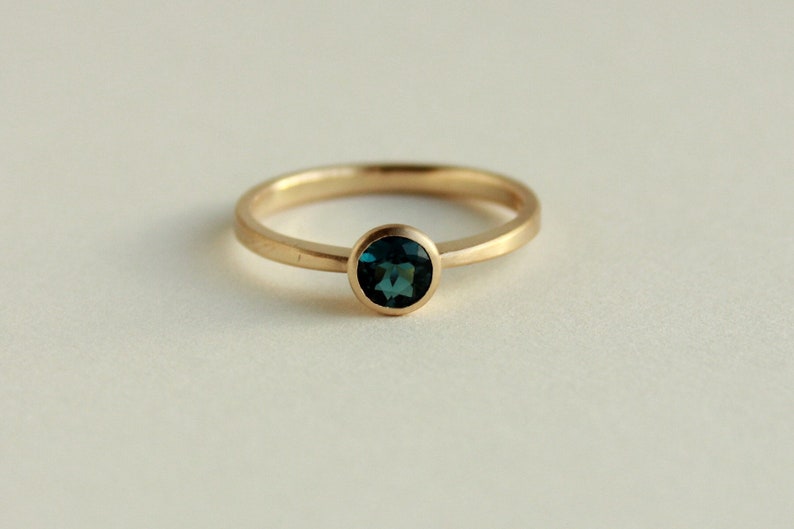 May include: A gold ring with a round, dark blue gemstone.