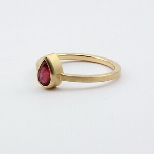 May include: A gold ring with a pear-shaped red gemstone.