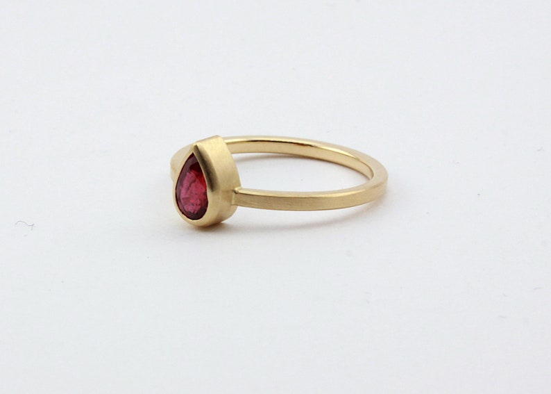 May include: A gold ring with a pear-shaped red gemstone.