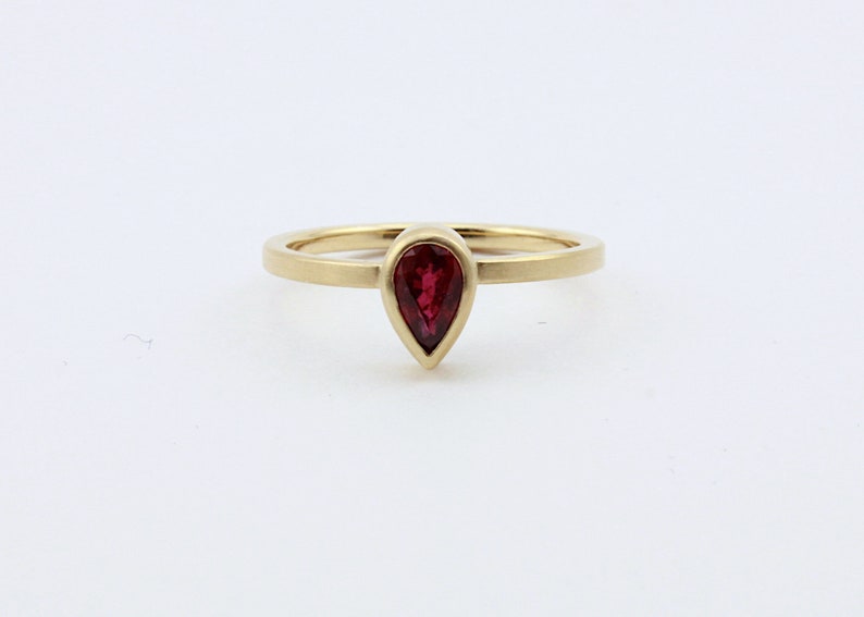 May include: A gold ring with a pear-shaped ruby gemstone.