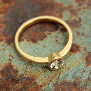 May include: A gold ring with a single, clear gemstone set in the center. The ring is on a rusty metal surface.