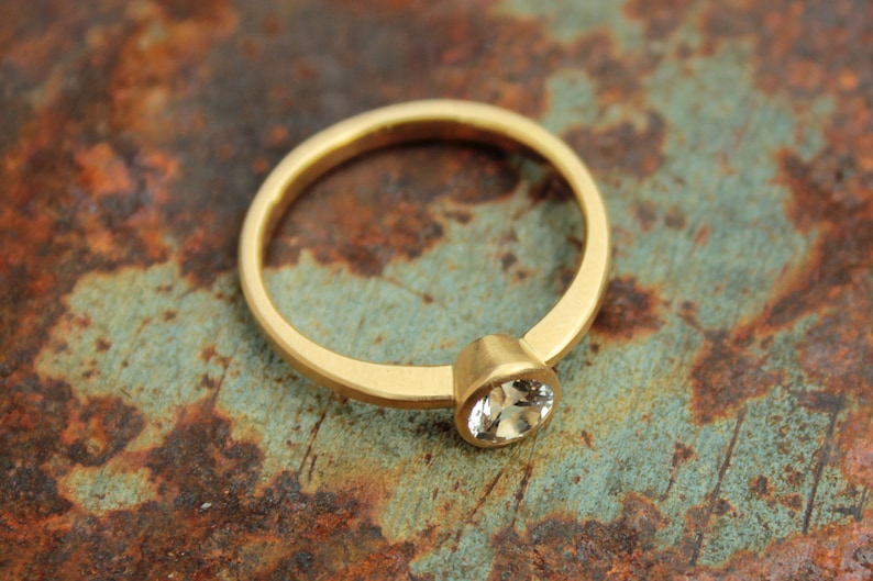 May include: A gold ring with a single, clear gemstone set in the center. The ring is on a rusty metal surface.