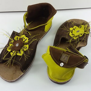 Puede incluir: Un par de sandalias de cuero marr&oacute;n y amarillo con un dise&ntilde;o floral. Las sandalias tienen una correa que va alrededor del tobillo y un cierre de hebilla.