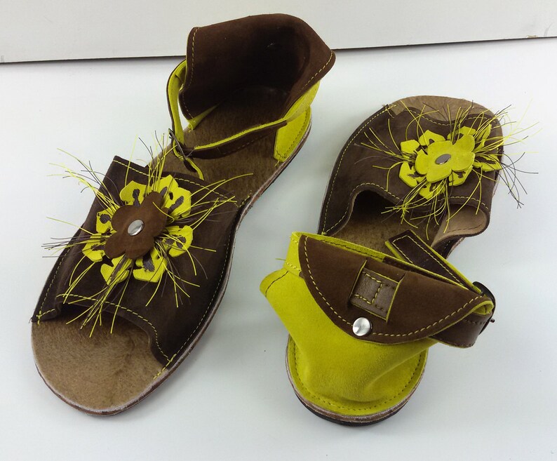 Puede incluir: Un par de sandalias de cuero marr&oacute;n y amarillo con un dise&ntilde;o floral. Las sandalias tienen una correa que va alrededor del tobillo y un cierre de hebilla.