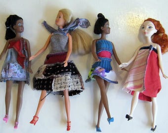 Puede incluir: Cuatro muñecas con diferentes vestidos coloridos hechos de tela reciclada. Las muñecas tienen el pelo largo y están en posición de pie.