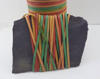 May include: A black slate stone with a bundle of colorful leather cords tied around it. The cords are red, green, yellow, and orange.
