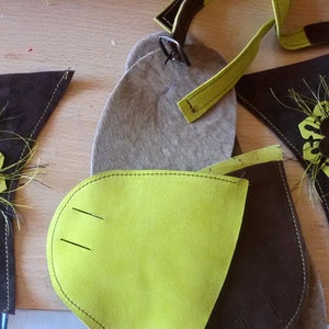 Puede incluir: Primer plano de piezas de cuero marr&oacute;n con detalles en fieltro verde. Las piezas tienen un dise&ntilde;o de flor con un bot&oacute;n marr&oacute;n en el centro. Las piezas est&aacute;n dispuestas sobre una superficie de madera con un tubo de pegamento.