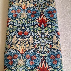Puede incluir: Tela doblada con un detallado estampado floral en tonos azul marino, rojo, amarillo y verde. El diseño presenta flores y follaje estilizados, creando una apariencia rica y ornamentada. La tela parece estar densamente tejida.