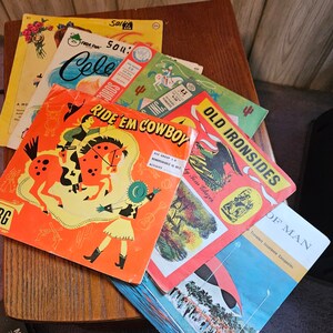 May include: A collection of vintage children's activity books with colorful illustrations. The books feature cowboys, horses, and other western themes. The titles include "Ride 'Em Cowboy", "Old Ironsides", and "Cele Sou's".