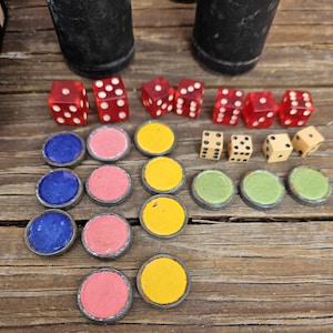 Könnte beinhalten: Ein Satz Spielsteine für ein Brettspiel. Die Spielsteine sind aus Holz und Kunststoff und in verschiedenen Farben erhältlich, darunter Rot, Blau, Gelb und Grün. Es gibt auch Würfel und eine Holzkiste.