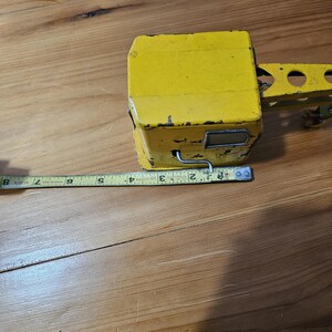 K&ouml;nnte beinhalten: Gelber Spielzeugkran aus Metall. Der Kran hat einen langen Arm und eine kleine Kabine. Der Kran steht auf einer Holzoberfl&auml;che.