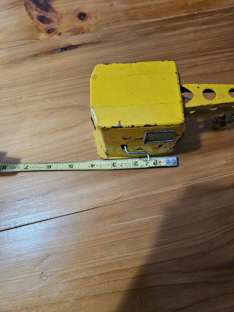 K&ouml;nnte beinhalten: Gelber Spielzeugkran aus Metall. Der Kran hat einen langen Arm und eine kleine Kabine. Der Kran steht auf einer Holzoberfl&auml;che.