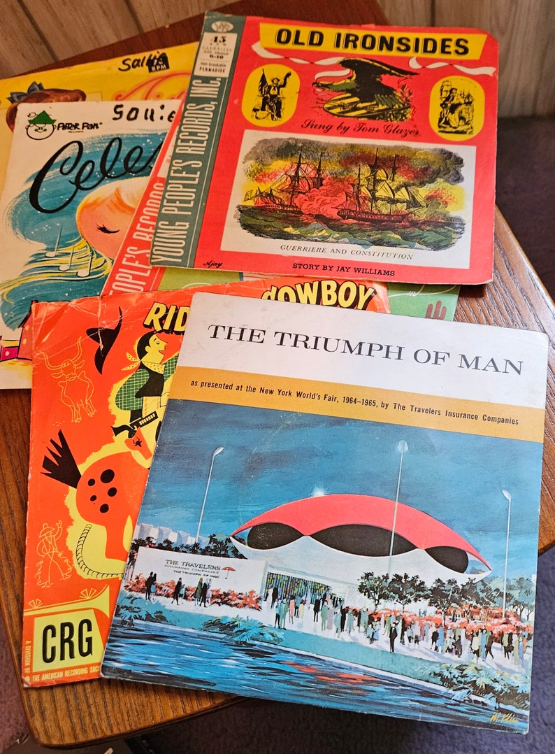 May include: A stack of five vintage children's records. The top record is red and features a picture of a ship with the title "Old Ironsides". The second record is orange and features a picture of a cowboy riding a horse with the title "Ride a Cowboy". The third record is blue and features a picture of a building with the title "The Triumph of Man". The fourth record is orange and features a picture of a horse with the title "Ride a Cowboy". The bottom record is red and features a picture of a celebration with the title "Celebrate".