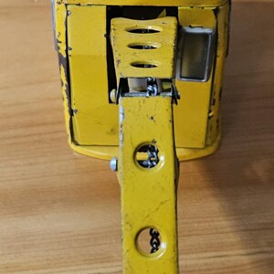 K&ouml;nnte beinhalten: Ein gelber Spielzeugkran mit einer Metallkette und einem beweglichen Arm. Der Kran hat ein kleines Fenster an der Seite und ist aus Metall.