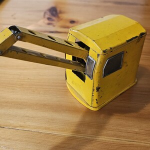 K&ouml;nnte beinhalten: Gelber Spielzeugkran aus Metall mit einem Gelenkarm. Der Kran hat eine kleine Kabine mit Fenstern und ist aus lackiertem Metall.