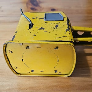K&ouml;nnte beinhalten: Gelber Spielzeugkran aus Metall mit einem grauen Fenster und einem silbernen Hebel. Dem Kran fehlt ein Teil seines Arms und er hat etwas Rost.