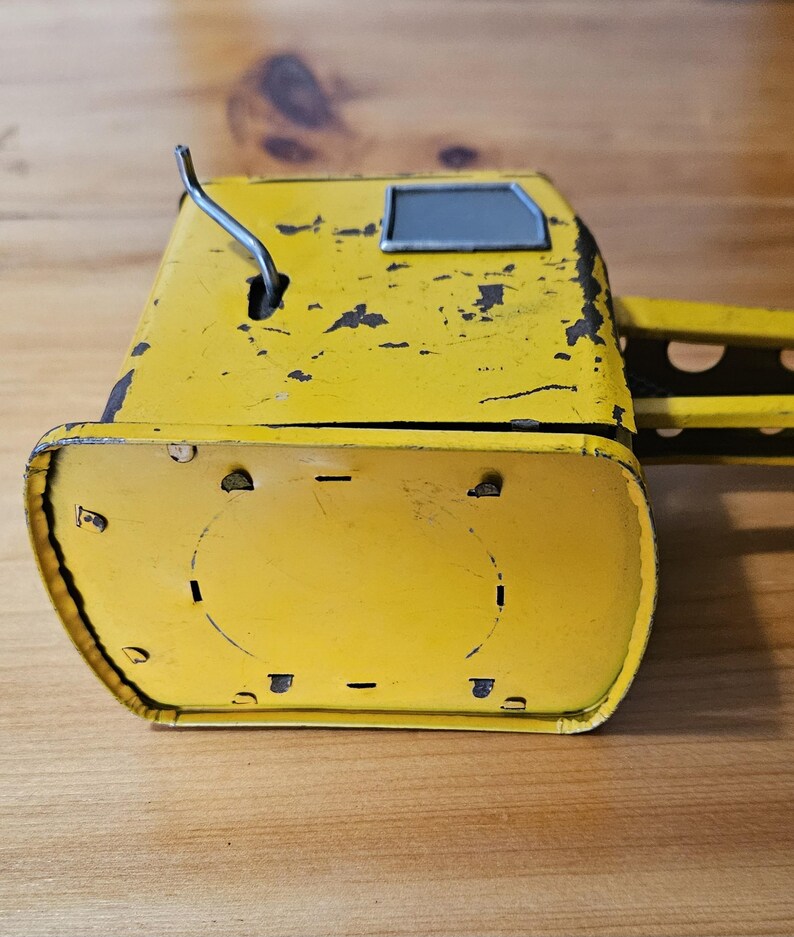K&ouml;nnte beinhalten: Gelber Spielzeugkran aus Metall mit einem grauen Fenster und einem silbernen Hebel. Dem Kran fehlt ein Teil seines Arms und er hat etwas Rost.