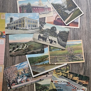 May include: A collection of vintage postcards featuring various scenes. The postcards depict buildings, landscapes, and historical sites, including Hershey Country Co., J.C. Blair Memorial Hospital, and Bonanza Manor. The postcards are arranged on a wooden surface.