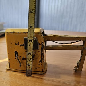 K&ouml;nnte beinhalten: Ein gelber Spielzeugkran mit einer Metallkette und einem Hebel. Der Kran ist etwa 13 cm hoch und aus Metall. Er hat einen abgenutzten, Vintage-Look.