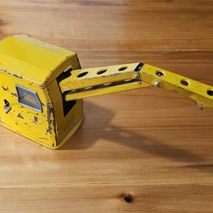 K&ouml;nnte beinhalten: Gelber Spielzeugkran mit einem Metallarm und einer Kabine. Der Kran ist aus Metall und hat einen verwitterten, Vintage-Look.