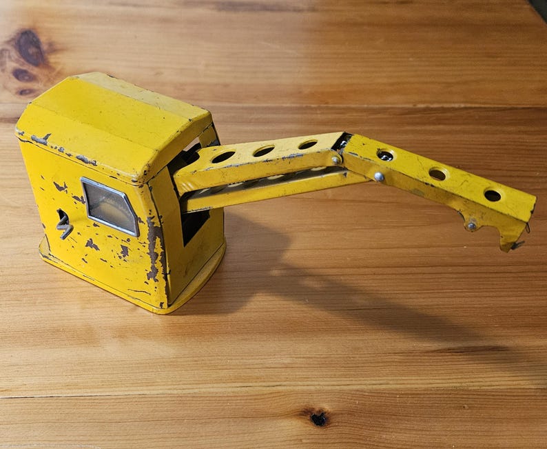 K&ouml;nnte beinhalten: Gelber Spielzeugkran mit einem Metallarm und einer Kabine. Der Kran ist aus Metall und hat einen verwitterten, Vintage-Look.