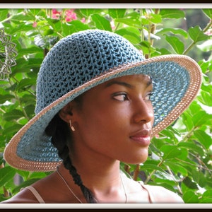 May include: A blue and beige crocheted sun hat with a wide brim. The hat is worn by a person with dark hair and brown skin.