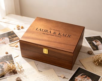 May include: A rectangular wooden keepsake box with a hinged lid and a gold-coloured metal latch. The lid is engraved with the text "Our Memories", "LAURA & KALIE", and "Est. December 27, 2025". The box features a smooth, dark brown wood grain finish.