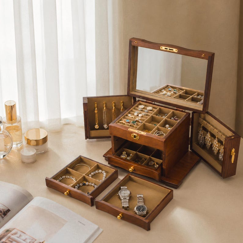 May include: A dark wood jewellery box with a hinged lid featuring an interior mirror, multiple open compartments, and side panels with hooks for hanging necklaces. The box includes two removable drawers with dividers for storing rings, bracelets, and two wristwatches.