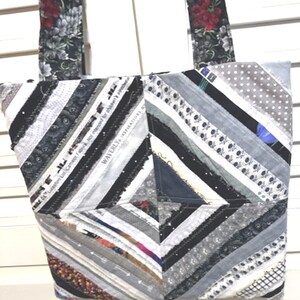 May include: A gray and black patchwork tote bag with a diagonal pattern. The bag has a black strap and is made of various fabrics, including denim, lace, and ribbon. The bag has the text "WAVERLY" and "INSPIRATIONS" printed on it.