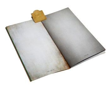 Puede incluir: Un libro abierto con páginas envejecidas de color blanquecino y un marcapáginas de metal dorado. Las páginas del libro tienen un aspecto texturizado y los bordes muestran una ligera decoloración marrón. El marcapáginas es rectangular con un diseño en relieve.