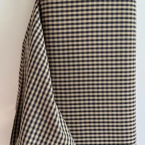 May include: A roll of fabric with a classic black and tan gingham pattern. The fabric is folded over, revealing the pattern and texture. The fabric is likely cotton or a similar material, suitable for sewing projects.