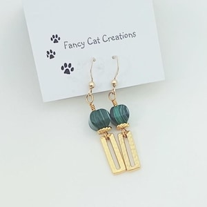 May include: Gold earrings with green malachite beads and gold rectangular charms. "Fancy Cat Creations" is written on a white card behind the earrings.