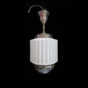 May include: Vintage ceiling light fixture with a white, ribbed glass shade and a silver-toned metal base. The light has a cylindrical shape and a decorative, textured bottom. The wires are visible at the top.