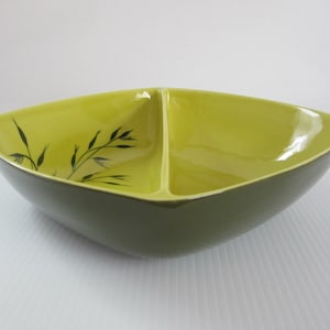 May include: A divided serving bowl with a square shape and a light green glaze. The bowl has a stylized leaf design in black on one side.