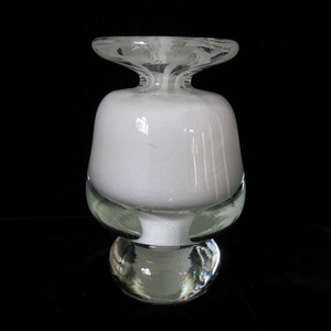 May include: A white glass vase with a wide, round base and a narrow, cylindrical neck. The vase has a textured, frosted finish and a clear glass base.