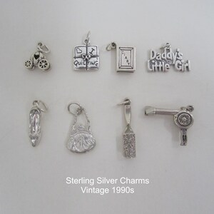 May include: A collection of nine vintage sterling silver charms from the 1990s. The charms include a carriage, a book with the word "Diary" on the cover, a book with the words "I Love Quilting" on the cover, a charm that says "Daddy's Little Girl", a high heel shoe, a purse, a hairbrush, and a hairdryer.