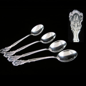 May include: Four silver spoons with ornate handles and oval bowls are displayed against a black background. A close-up of a spoon handle shows a detailed relief of a figure. The spoons are likely for serving or eating.