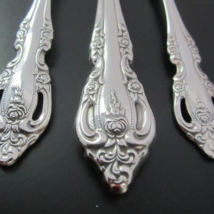 May include: Close-up of three silver spoons with ornate, floral designs. The spoons have a detailed, embossed pattern of roses and leaves.