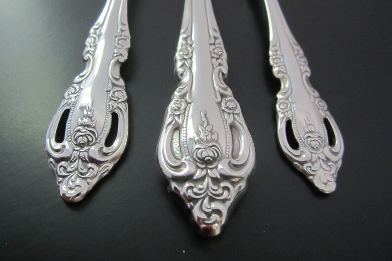 May include: Close-up of three silver spoons with ornate, floral designs. The spoons have a detailed, embossed pattern of roses and leaves.