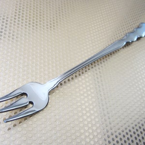 May include: A silver fork with a decorative handle. The fork has three tines and is designed for serving food.
