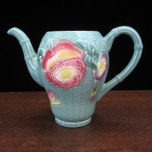 May include: A light blue ceramic teapot with a floral design. The teapot has a handle and a spout. The flowers are pink, yellow, and purple.