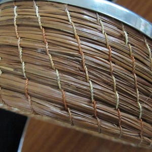 May include: A woven basket with a silver metal rim. The basket is made of natural brown fibres and has a woven pattern with white and orange threads.