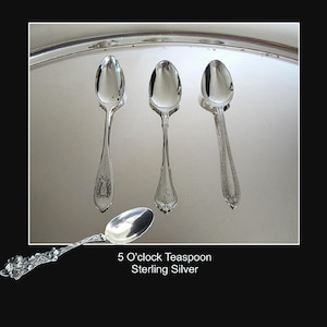 May include: Four silver spoons with polished bowls and decorative handles. Three spoons are arranged vertically, while one is positioned horizontally at the bottom. The text 5 O'clock Teaspoon Sterling Silver is printed below the spoons.