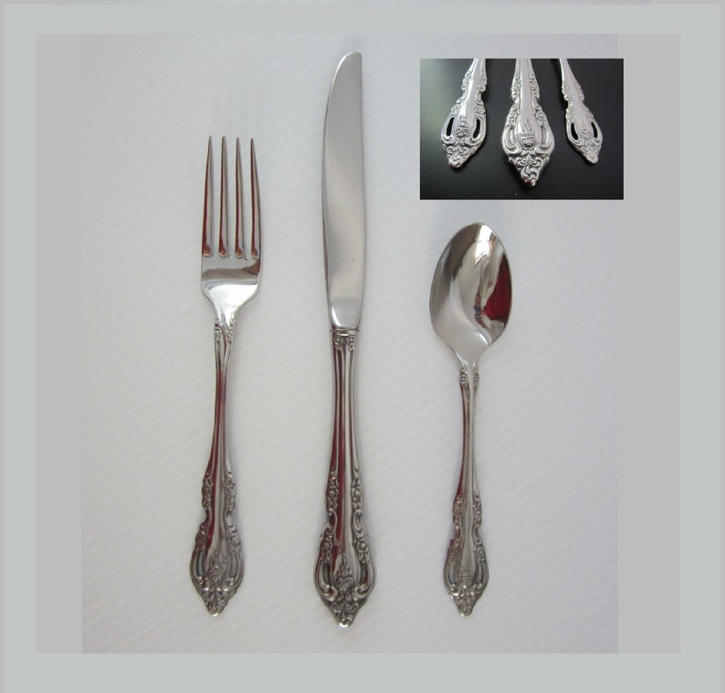 May include: A set of three silver-toned flatware pieces: a fork, a knife, and a spoon. The pieces have an ornate, decorative design.